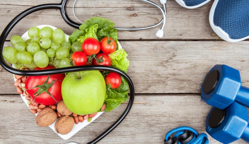 top view of stethoscope, organic vegetables and fruits and sport equipment on wooden surface,